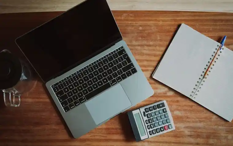 책상 위에 놓인 노트북과 계산기, 펼쳐진 메모지