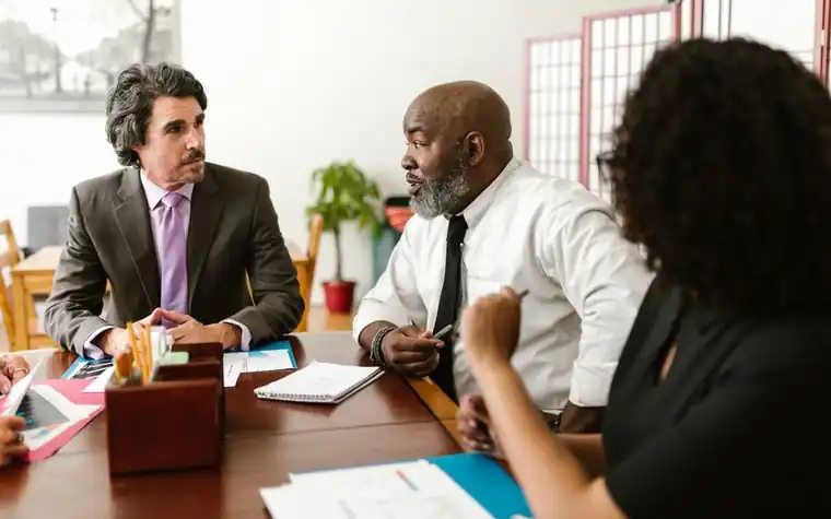 회의 테이블에 마주 앉아 서류를 보며 논의하는 세 사람